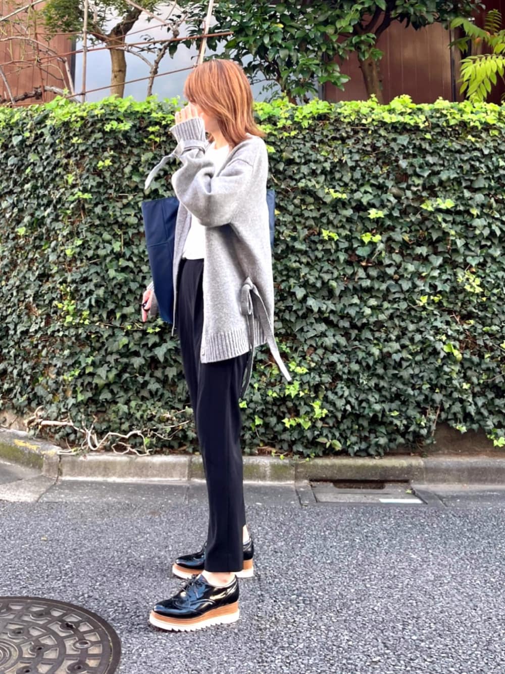 グリーン系のトートバッグ、ホワイト系のTシャツ/カットソー、グレー系のニット/セーターを着用したレディースの秋コーディネートの4枚目の写真