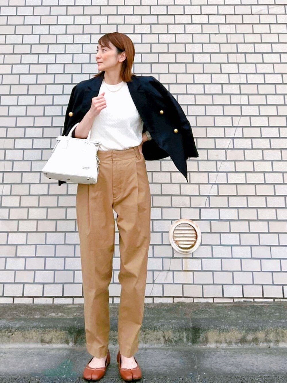 イエロー系のチノパンツ、ホワイト系のハンドバッグ、ブルー系のテーラードジャケットを着用したレディースの春コーディネートの3枚目の写真