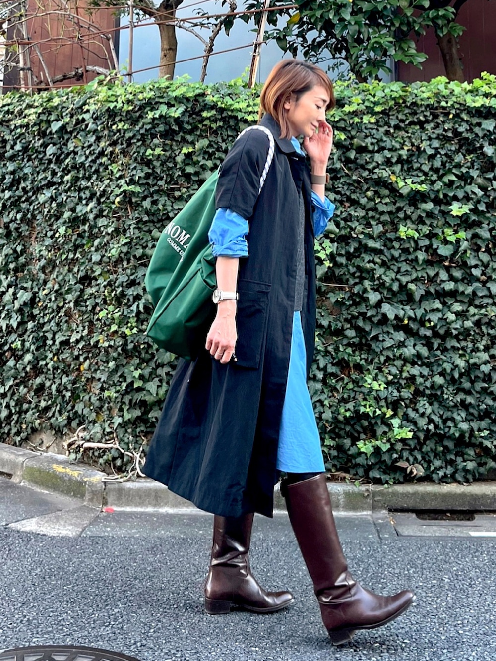 グリーン系のトートバッグ、ブラック系のステンカラーコート、ブルー系のシャツ/ブラウスを着用したレディースの秋コーディネートの2枚目の写真