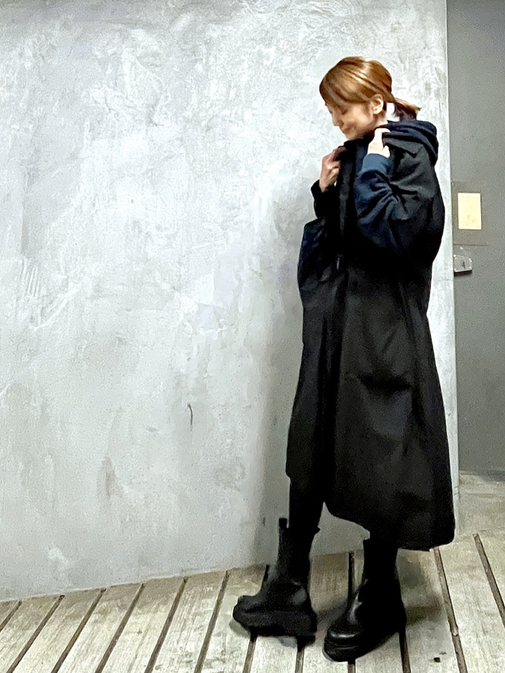 ブラック系のステンカラーコート、ブルー系のパーカー、ブラック系のブーツを着用したレディースの秋コーディネートの3枚目の写真