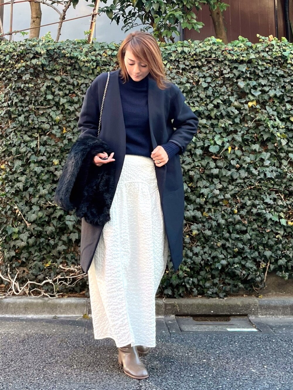 グリーン系のショルダーバッグ、ブルー系のニット/セーター、ホワイト系のスカートを着用したレディースの冬コーディネートの2枚目の写真