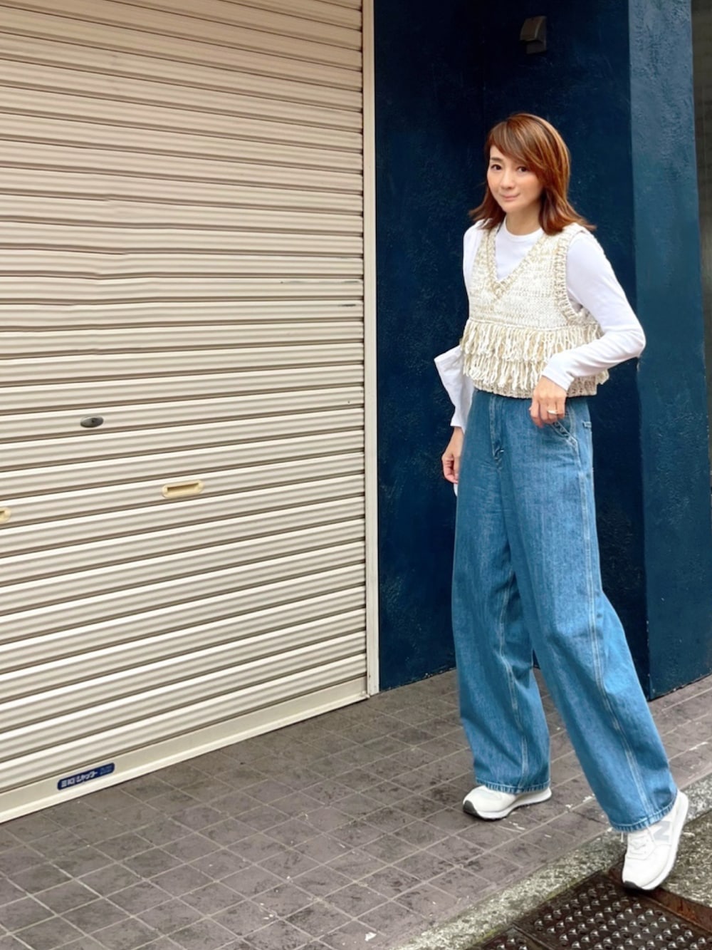 ホワイト系のベスト、ブルー系のデニムパンツ、ホワイト系のスニーカーを着用したレディースの春コーディネートの2枚目の写真