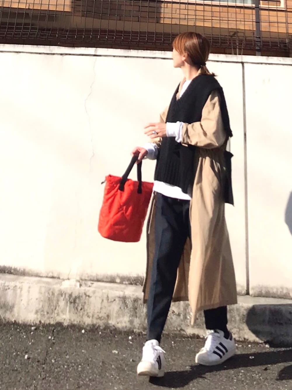 オレンジ系のトートバッグ、ブラック系のニット/セーター、ベージュ系のワンピースを着用したレディースの春コーディネートの2枚目の写真