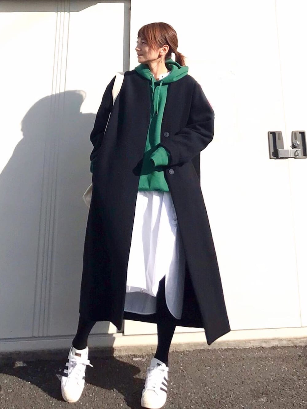 ブラック系のノーカラーコート、グリーン系のパーカー、ホワイト系のワンピースを着用したレディースの冬コーディネートの2枚目の写真
