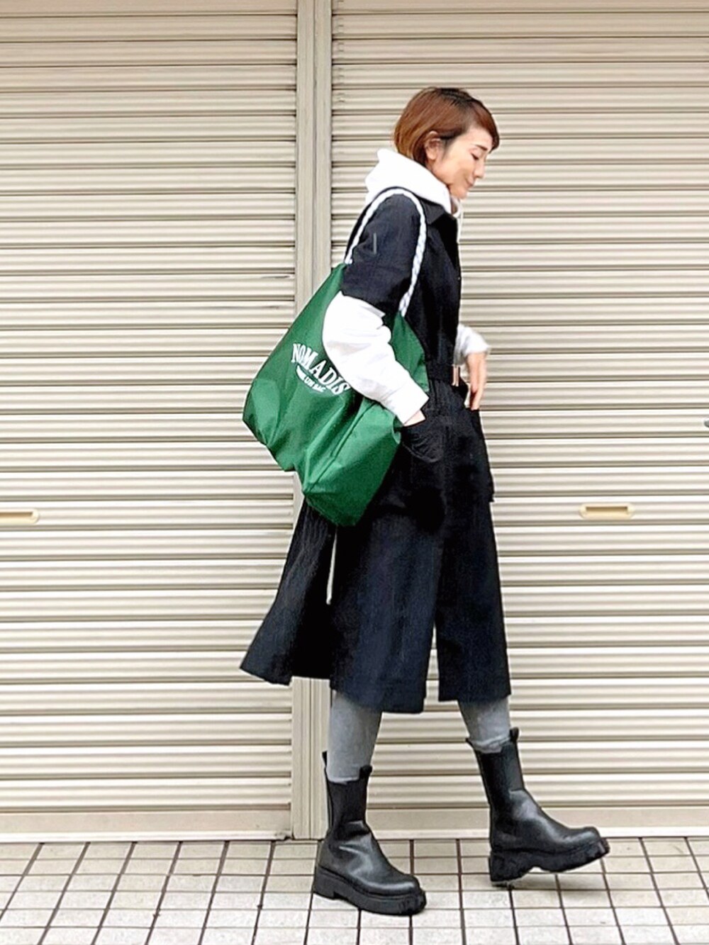 ブラック系のステンカラーコート、ブラック系のブーツ、ホワイト系のTシャツ/カットソーを着用したレディースの秋コーディネートの2枚目の写真