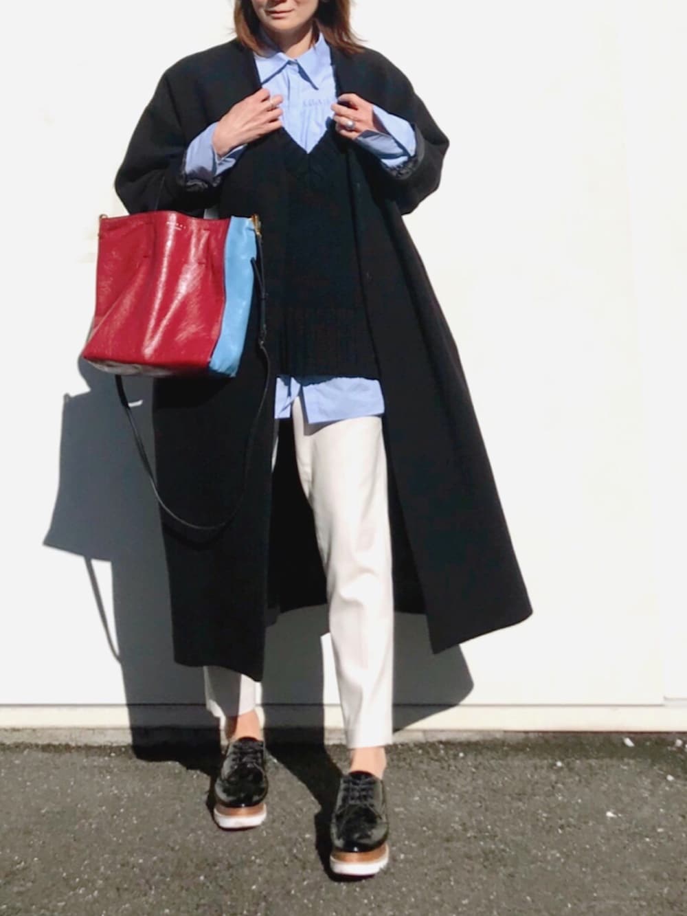 ブラック系のノーカラーコート、ブルー系のシャツ/ブラウス、ブラック系のニット/セーターを着用したレディースの冬コーディネートの2枚目の写真