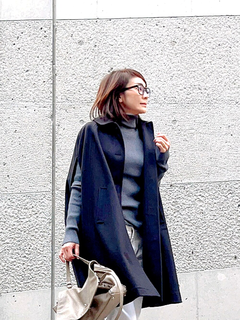 グレー系のニット/セーター、ブルー系のポンチョ、グレー系のハンドバッグを着用したレディースの秋コーディネートの3枚目の写真