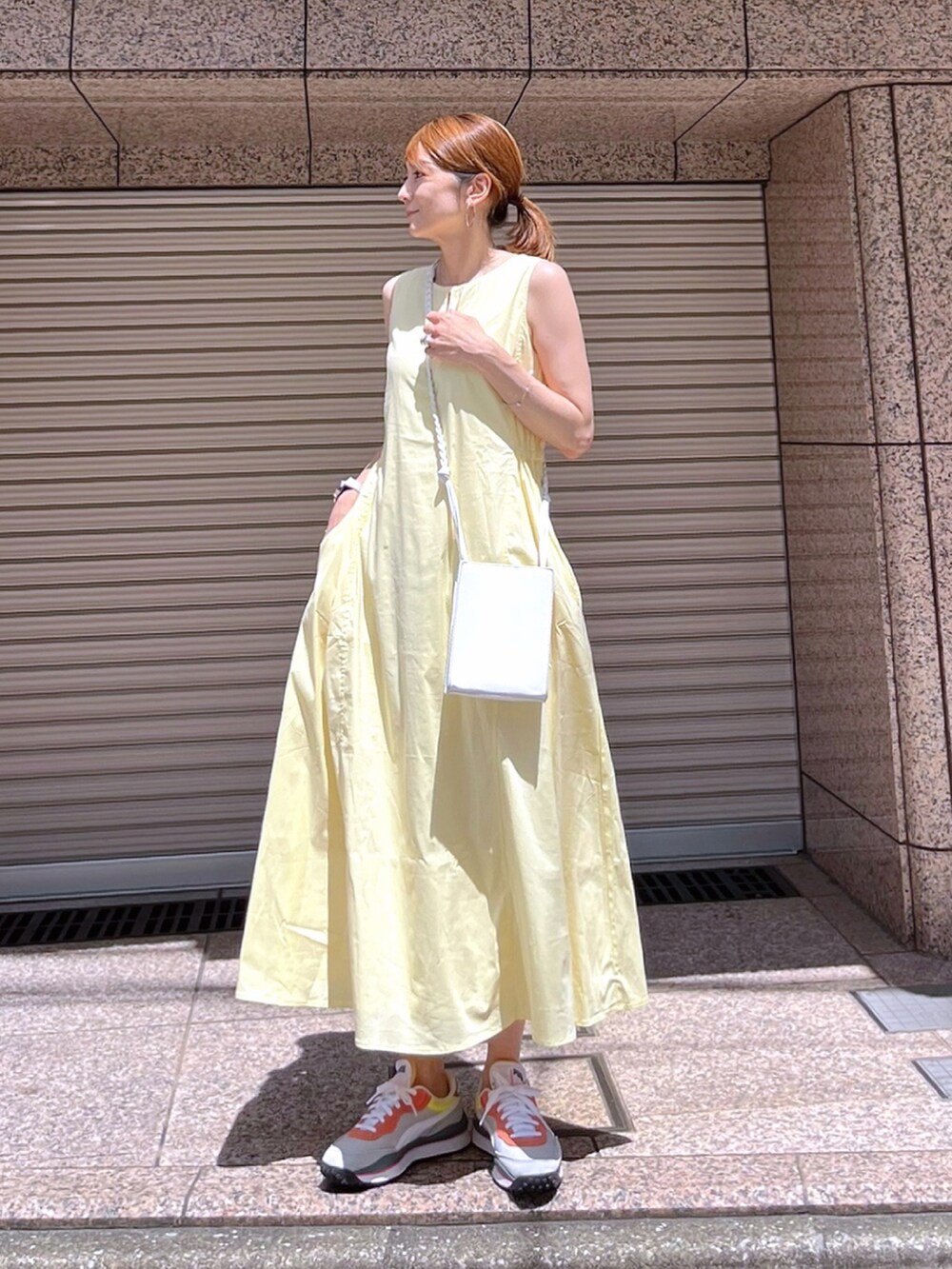イエロー系のワンピース、ホワイト系のショルダーバッグ、グレー系のスニーカーを着用したレディースの夏コーディネートの2枚目の写真