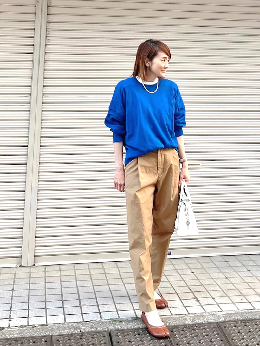 イエロー系のチノパンツ、ブルー系のニット/セーター、ホワイト系のハンドバッグを着用したレディースの春コーディネートの3枚目の写真