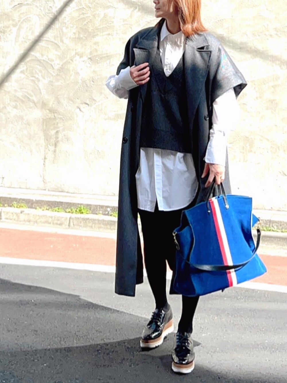 グレー系のチェスターコート、ホワイト系のシャツ/ブラウス、ブルー系のトートバッグを着用したレディースの春コーディネートの2枚目の写真
