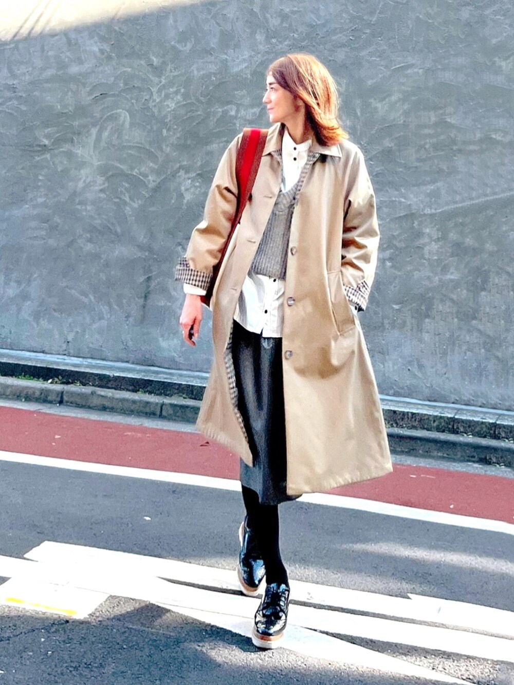 ベージュ系のステンカラーコート、ホワイト系のシャツ/ブラウス、グリーン系のスカートを着用したレディースの秋コーディネートの2枚目の写真