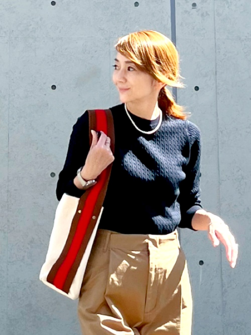 イエロー系のチノパンツ、ブルー系のニット/セーター、ブラウン系のショルダーバッグを着用したレディースの秋コーディネートの2枚目の写真