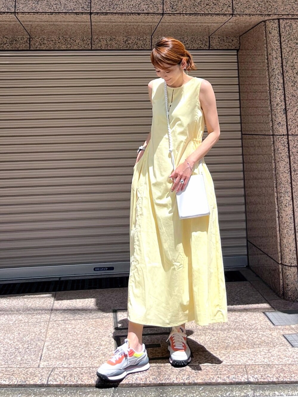 イエロー系のワンピース、ホワイト系のショルダーバッグ、グレー系のスニーカーを着用したレディースの夏コーディネートの3枚目の写真