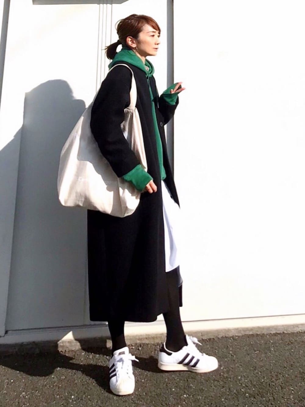 ブラック系のノーカラーコート、グリーン系のパーカー、ホワイト系のワンピースを着用したレディースの冬コーディネートの3枚目の写真