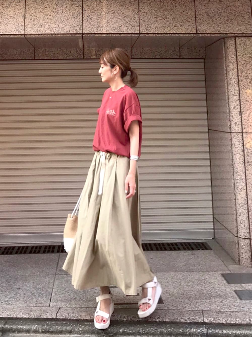 レッド系のTシャツ/カットソー、ベージュ系のスカート、ホワイト系のショルダーバッグを着用したレディースの夏コーディネートの3枚目の写真
