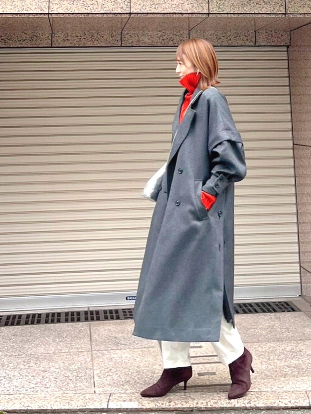 グレー系のチェスターコート、オレンジ系のニット/セーター、ホワイト系のその他パンツを着用したレディースの冬コーディネートの2枚目の写真