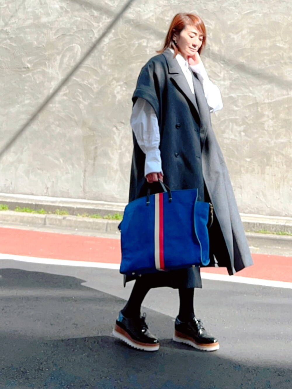 グレー系のチェスターコート、ホワイト系のシャツ/ブラウス、ブルー系のトートバッグを着用したレディースの春コーディネートの3枚目の写真