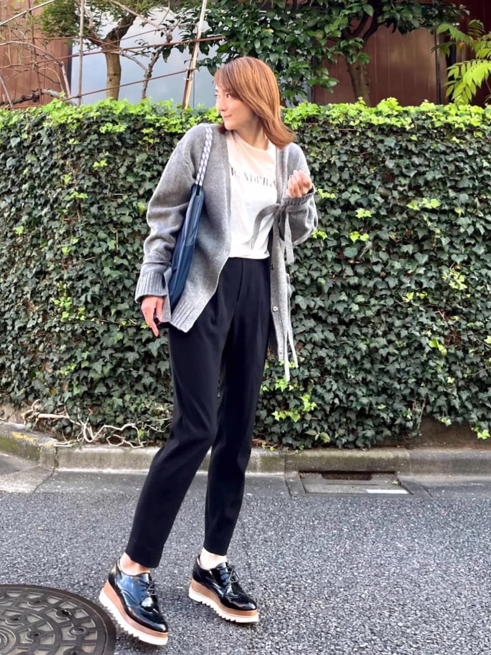 グリーン系のトートバッグ、ホワイト系のTシャツ/カットソー、グレー系のニット/セーターを着用したレディースの秋コーディネートの3枚目の写真