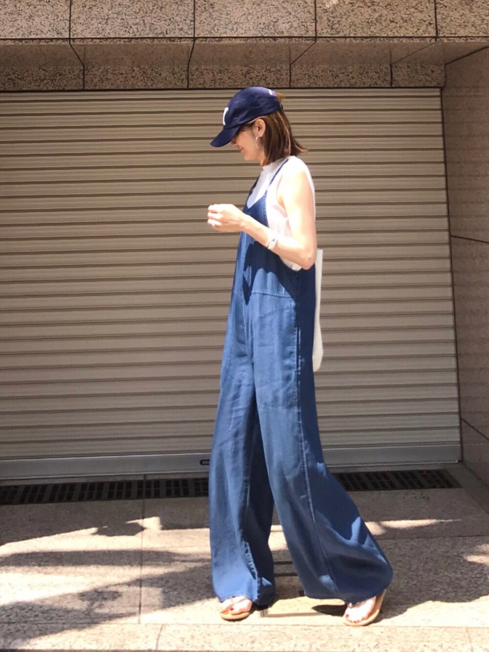 ホワイト系のトートバッグ、ブルー系のサロペット/オーバーオール、ゴールド系のサンダルを着用したレディースの夏コーディネートの3枚目の写真