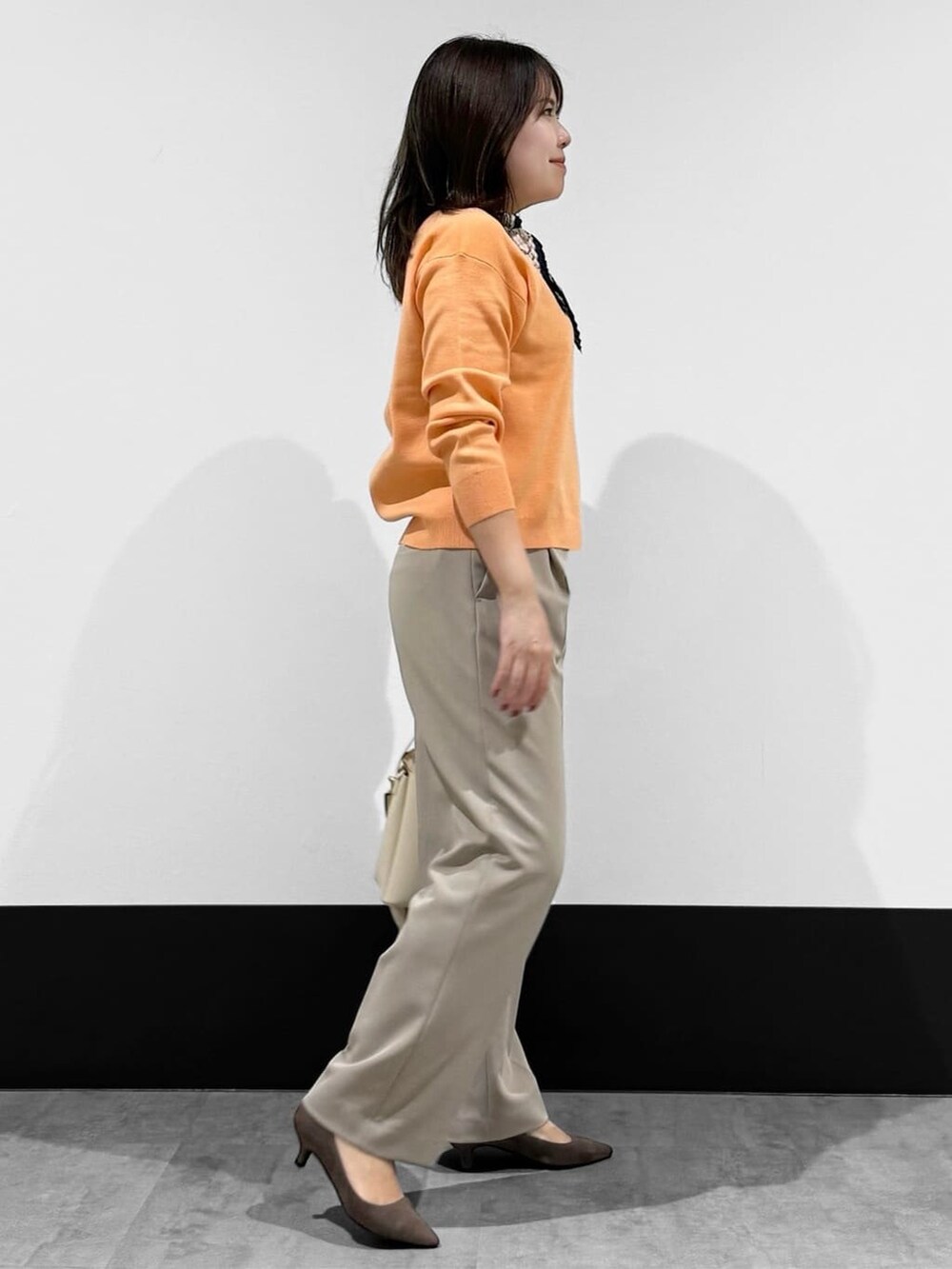 オレンジ系のニット/セーター、ベージュ系のその他パンツ、ホワイト系のハンドバッグを着用したレディースの春コーディネートの2枚目の写真