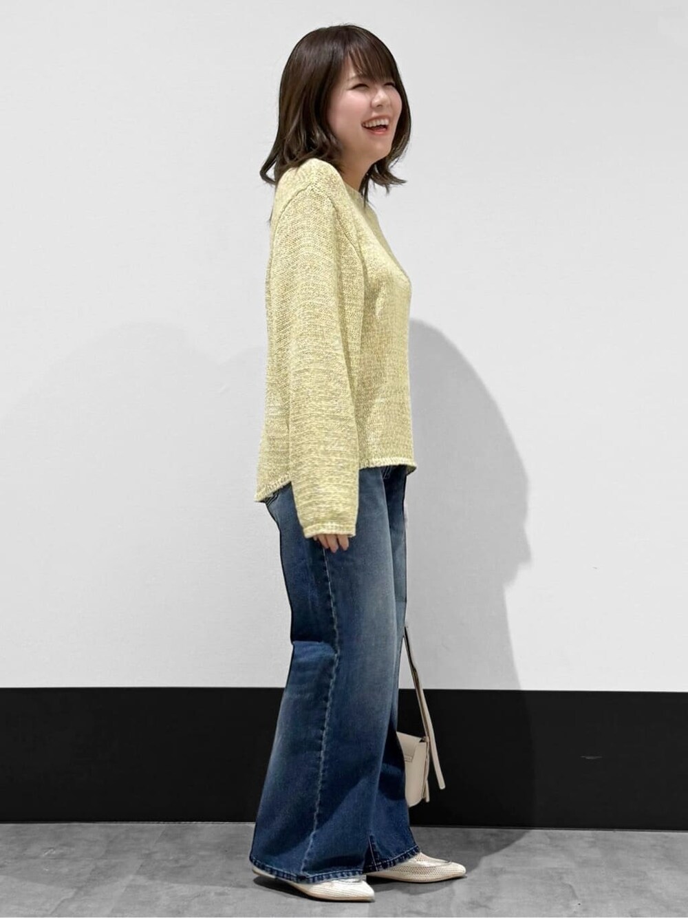 イエロー系のニット/セーター、ブルー系のデニムパンツ、ベージュ系のショルダーバッグを着用したレディースの春コーディネートの2枚目の写真