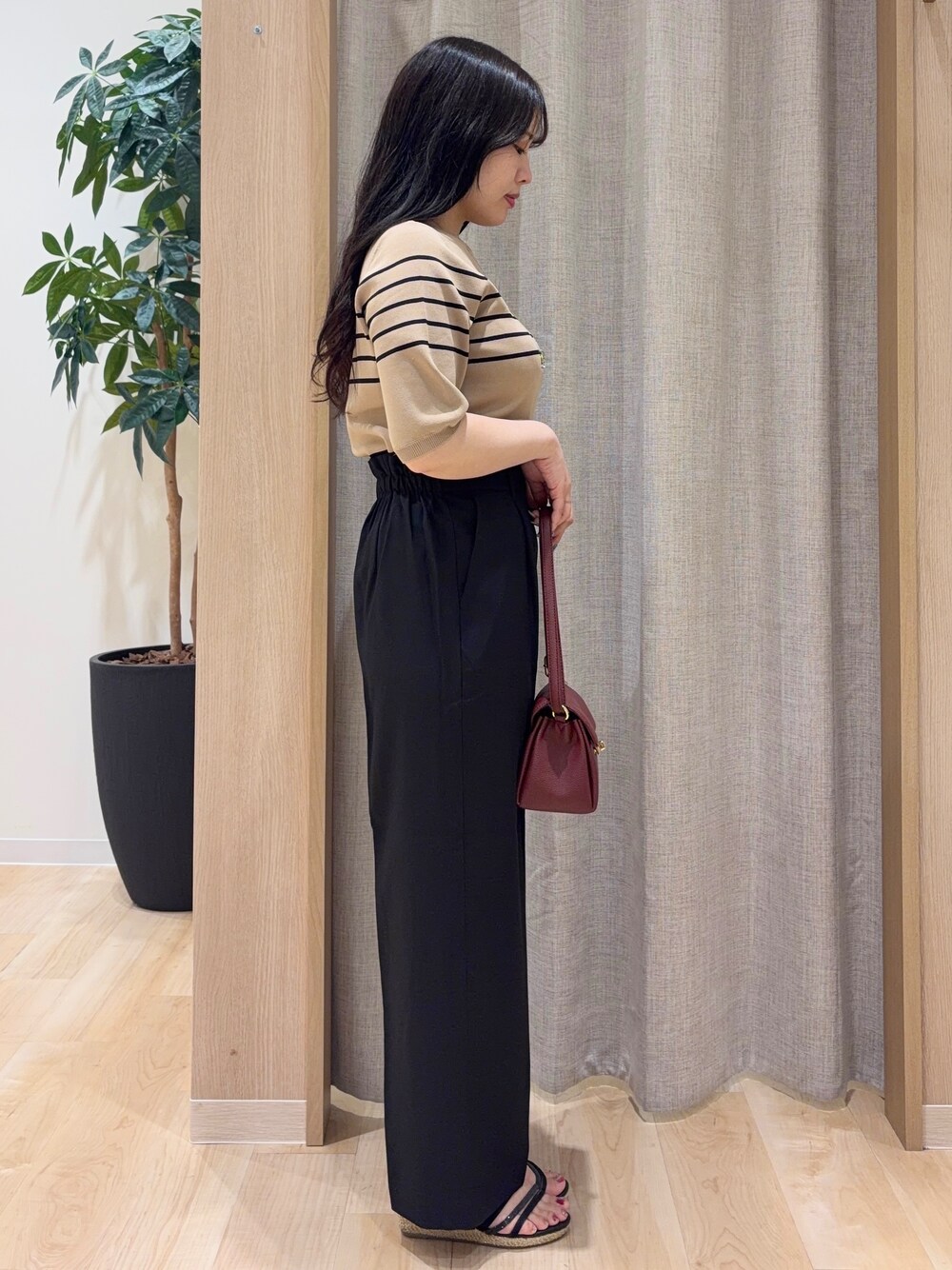 ベージュ系のニット/セーター、ブラック系のその他パンツ、レッド系のショルダーバッグを着用したレディースの夏コーディネートの2枚目の写真
