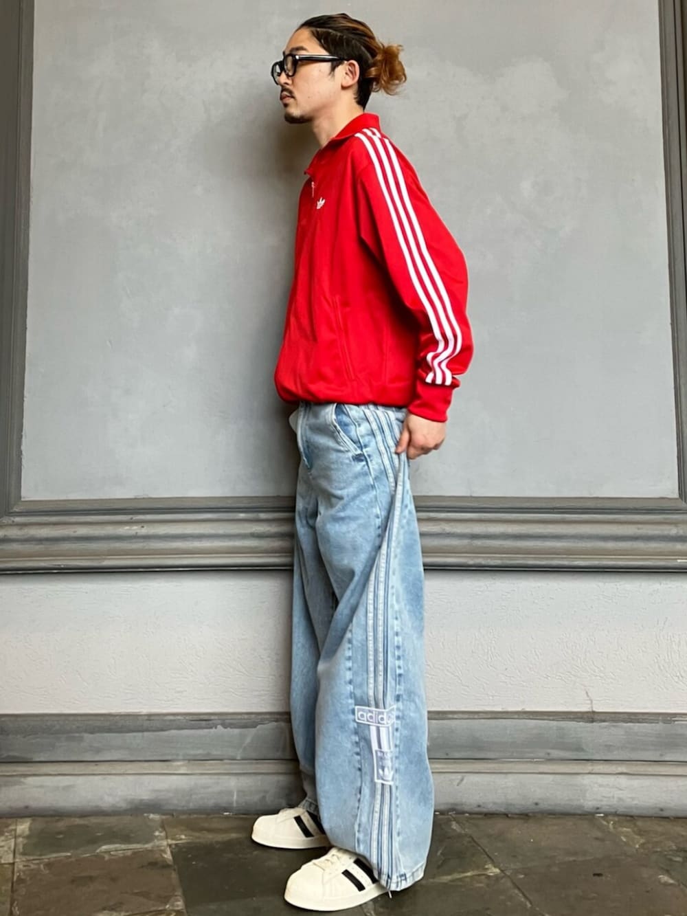 レッド系のジャージ、ブルー系のデニムパンツ、ホワイト系のスニーカーを着用したメンズの夏コーディネートの2枚目の写真