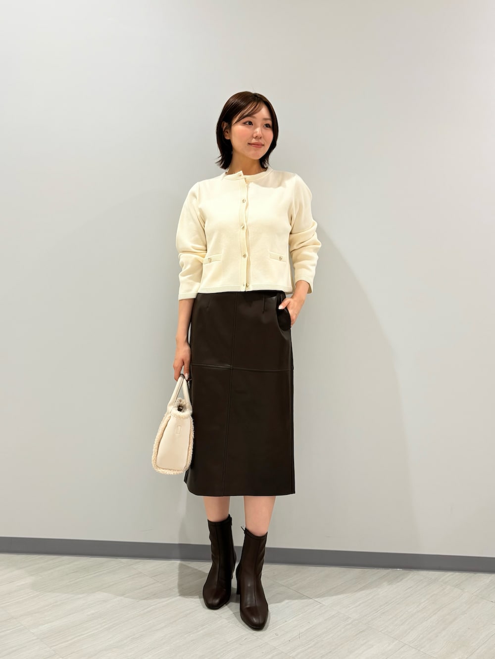 ホワイト系のカーディガン/ボレロ、ブラウン系のスカート、ブラウン系のブーツを着用したレディースの秋コーディネートの3枚目の写真