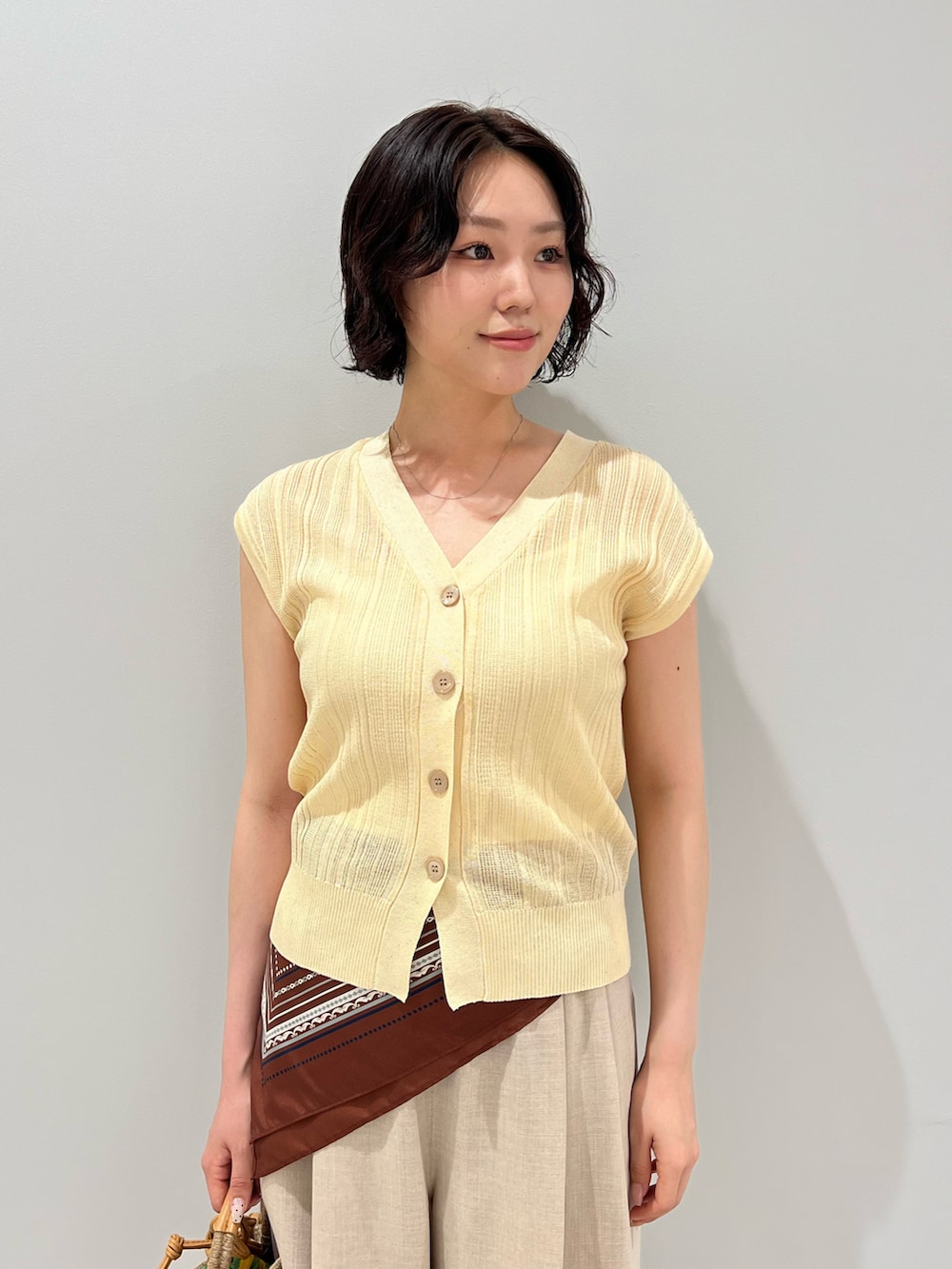 ベージュ系のショルダーバッグ、イエロー系のニット/セーター、ベージュ系のパンツを着用したレディースの夏コーディネートの5枚目の写真