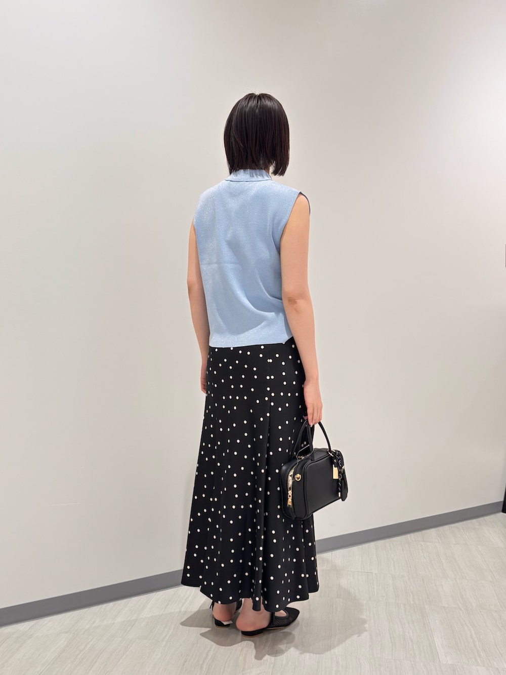 ブルー系のポロシャツ、ブラック系のスカート、ブラック系のボストンバッグを着用したレディースの夏コーディネートの4枚目の写真