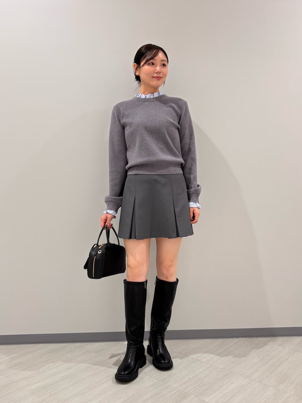 グレー系のニット/セーター、グレー系のスカート、ブラック系のボストンバッグを着用したレディースの秋コーディネートの2枚目の写真