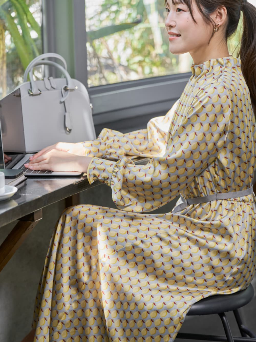 イエロー系のワンピース、グレー系のハンドバッグ、ゴールド系のイヤリングを着用したレディースの秋コーディネートの3枚目の写真