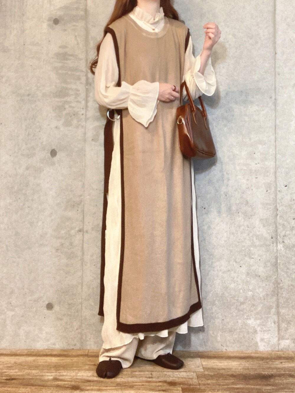 ブラウン系のベスト、ホワイト系のワンピース、ブラウン系のハンドバッグを着用したレディースの秋コーディネートの2枚目の写真