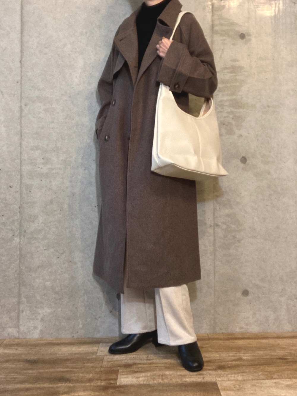 ブラウン系のチェスターコート、ブラック系のTシャツ/カットソー、ホワイト系のボストンバッグを着用したレディースの秋コーディネートの2枚目の写真