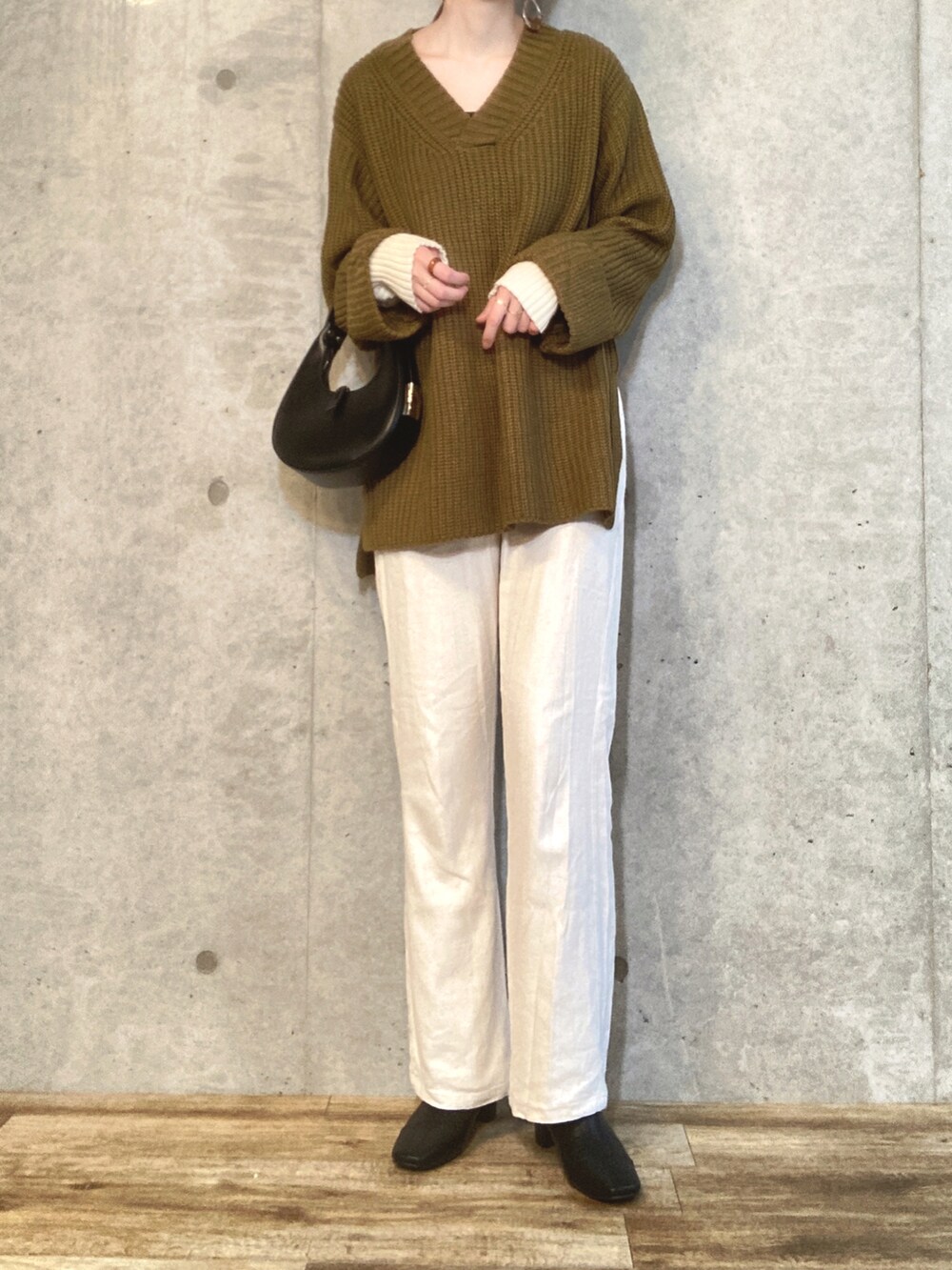 グリーン系のニット/セーター、ブラック系のハンドバッグ、ホワイト系のスラックスを着用したレディースの秋コーディネートの2枚目の写真