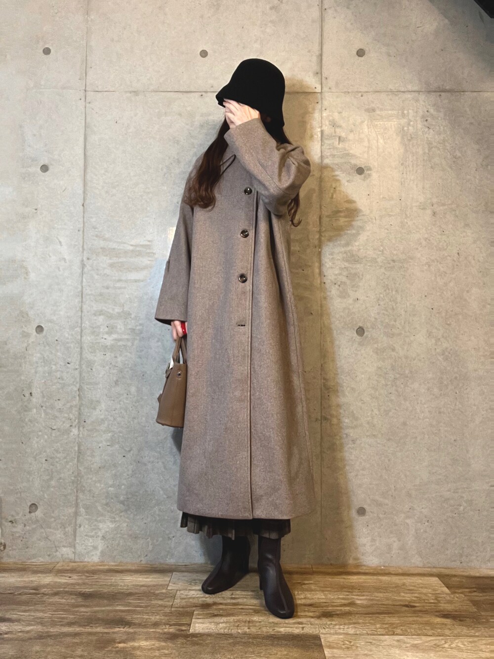 ブラウン系のステンカラーコート、ブラウン系のハンドバッグ、ブラウン系のブーツを着用したレディースの冬コーディネートの2枚目の写真