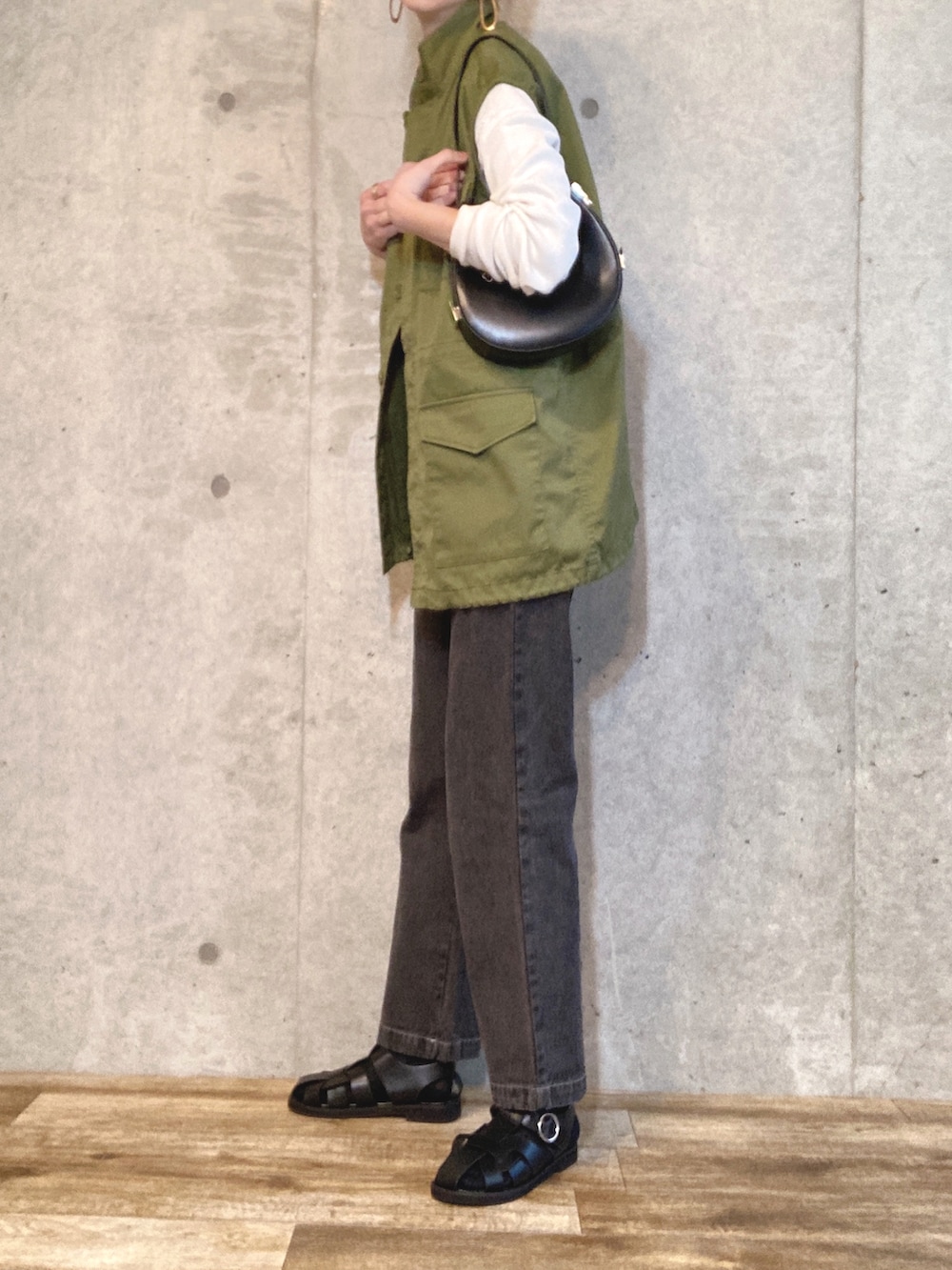 グリーン系のベスト、ブラック系のハンドバッグ、ブラック系のデニムパンツを着用したレディースの春コーディネートの2枚目の写真