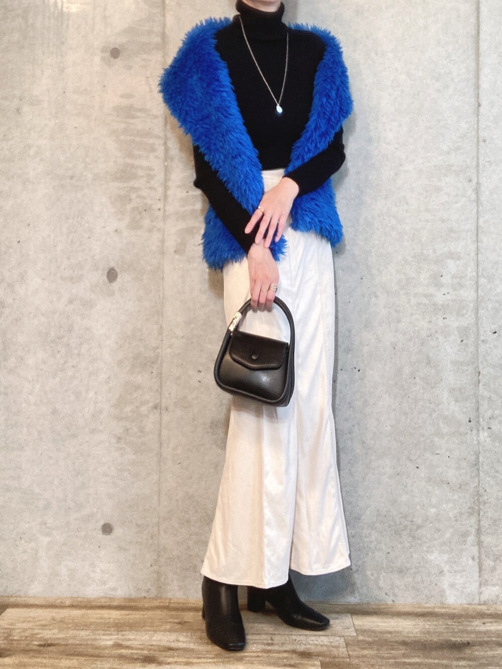 ブルー系のベスト、ブラック系のショルダーバッグ、ホワイト系のスカートを着用したレディースの秋コーディネートの2枚目の写真