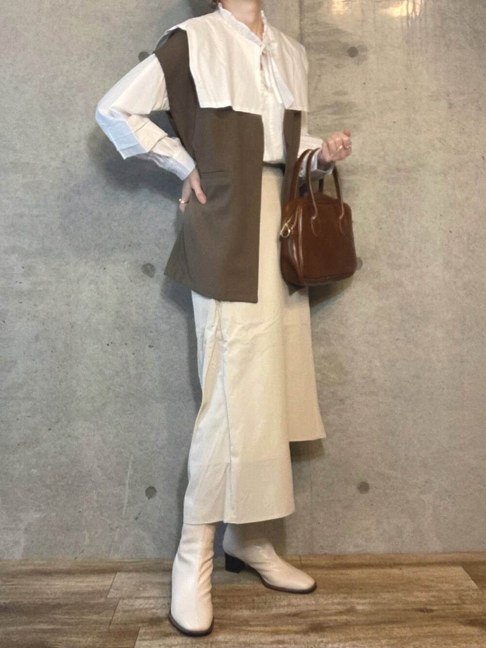 ホワイト系のシャツ/ブラウス、グリーン系のベスト、ブラウン系のハンドバッグを着用したレディースの春コーディネートの2枚目の写真