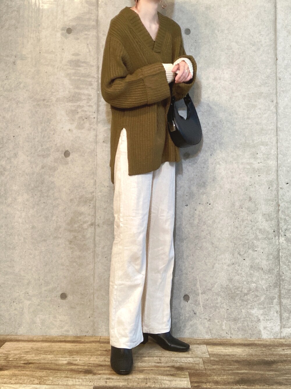 グリーン系のニット/セーター、ブラック系のハンドバッグ、ホワイト系のスラックスを着用したレディースの秋コーディネートの3枚目の写真