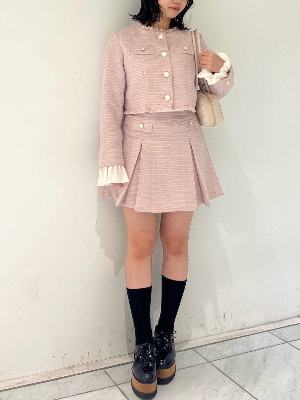 ピンク系のノーカラージャケット、ピンク系のスカート、イエロー系のハンドバッグを着用したレディースの冬コーディネートの2枚目の写真