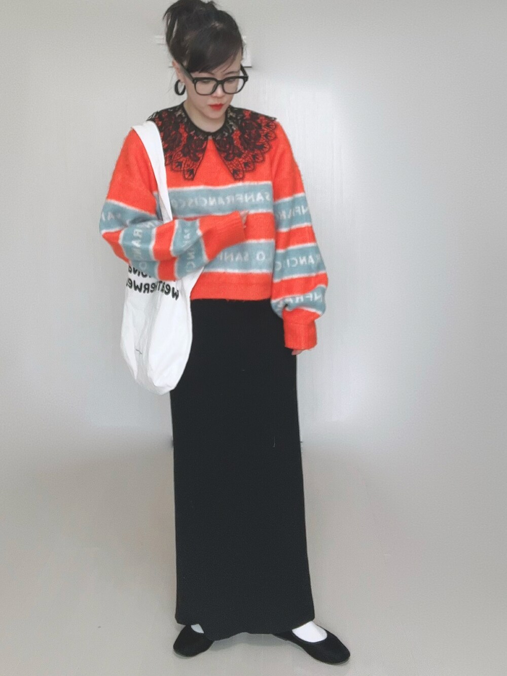 オレンジ系のニット/セーター、ホワイト系のトートバッグ、ブラック系のスカートを着用したレディースの冬コーディネートの3枚目の写真