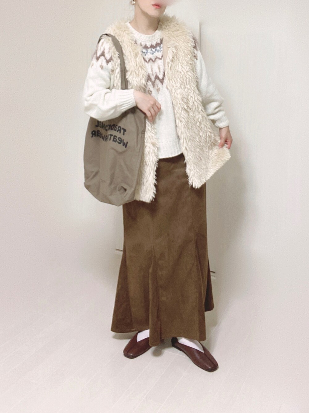 ホワイト系のベスト、ホワイト系のニット/セーター、ブラウン系のスカートを着用したレディースの秋コーディネートの3枚目の写真