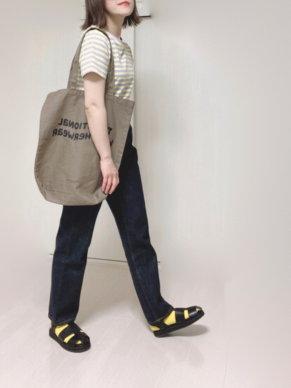 ブラック系のサンダル、ブラウン系のトートバッグ、ブルー系のデニムパンツを着用したレディースの夏コーディネートの4枚目の写真