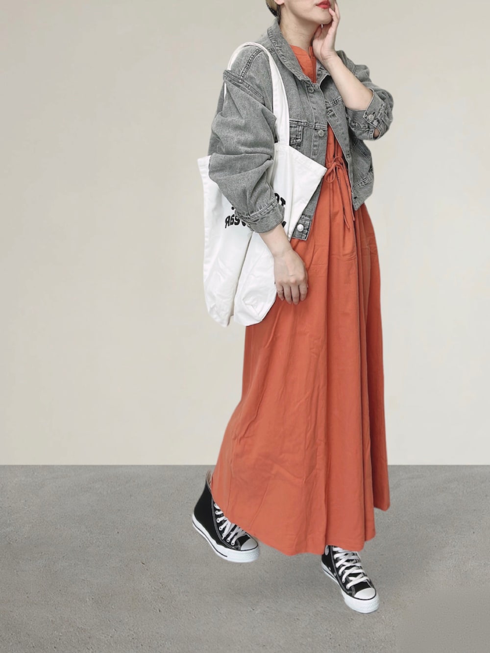 ブラック系のデニムジャケット、オレンジ系のワンピース、ホワイト系のトートバッグを着用したレディースの秋コーディネートの4枚目の写真