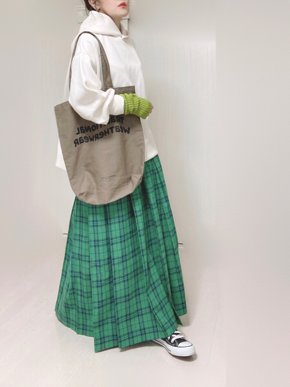ホワイト系のパーカー、ブラウン系のトートバッグ、グリーン系のスカートを着用したレディースの秋コーディネートの5枚目の写真