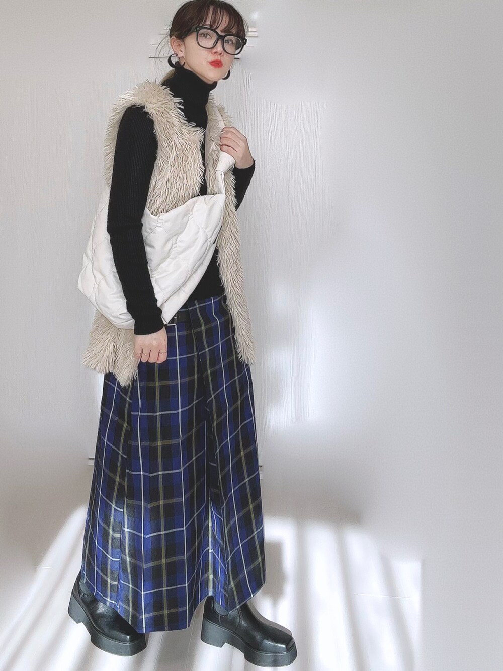 ホワイト系のベスト、ホワイト系のショルダーバッグ、ブラック系のブーツを着用したレディースの冬コーディネートの2枚目の写真