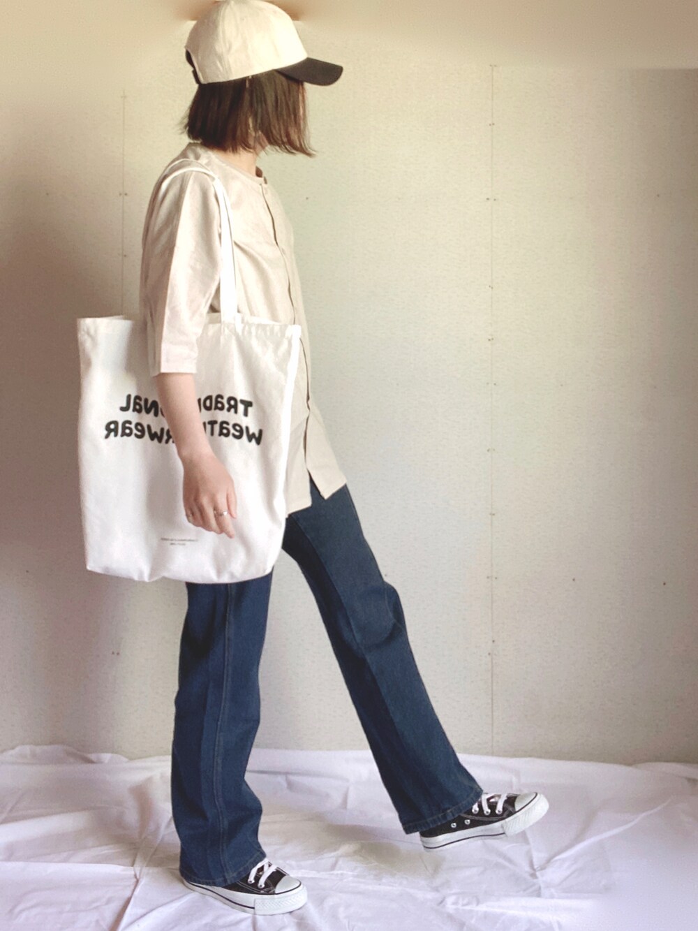 ホワイト系のトートバッグ、ベージュ系のチュニック、ブルー系のデニムパンツを着用したレディースの夏コーディネートの2枚目の写真