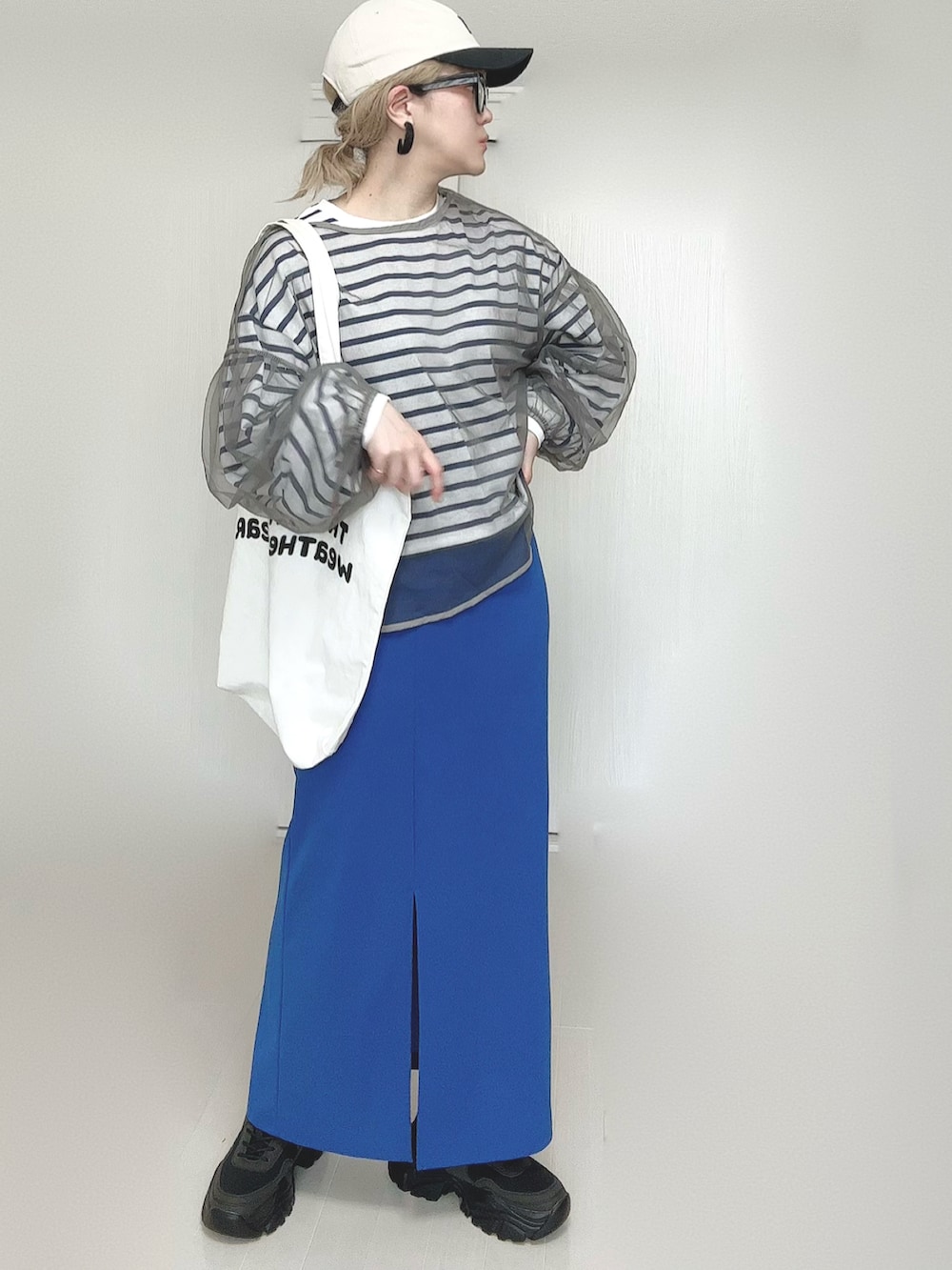 ブルー系のスカート、ホワイト系のトートバッグ、ブラック系のスニーカーを着用したレディースの春コーディネートの2枚目の写真