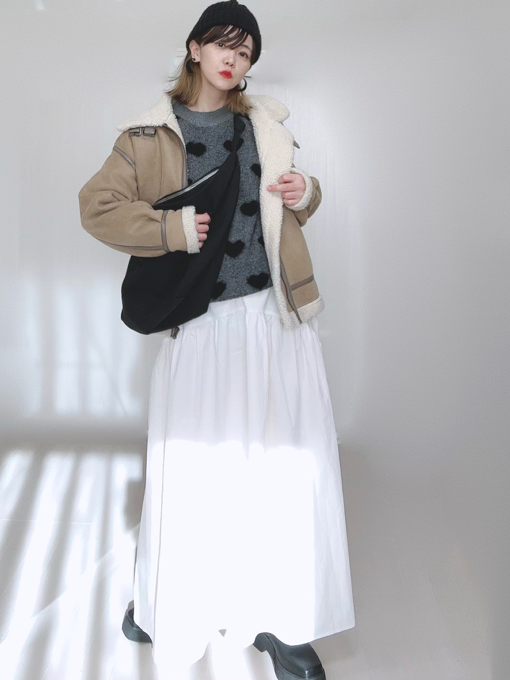ベージュ系のムートンコート、ホワイト系のスカート、ブラック系のブーツを着用したレディースの冬コーディネートの2枚目の写真